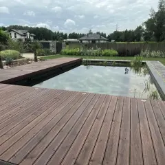 Drewniany taras otacza nowoczesny staw kąpielowy z roślinnością. Idealne miejsce na relaks w ogrodzie.