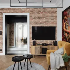 Nowoczesny salon z ceglaną ścianą, na której wisi telewizor. Oświetlenie podkreśla fakturę cegły, tworząc przytulną atmosferę.