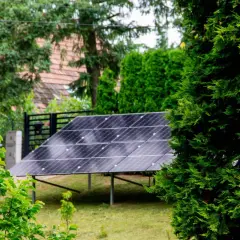 Panele fotowoltaiczne w ogrodzie, otoczone zielenią, czerpią energię ze słońca.