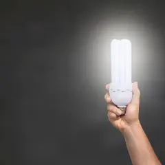 Dłoń trzymająca energooszczędną żarówkę, która świeci jasno. Zastanawiasz się, ile lumenów na m2 zapewni?
