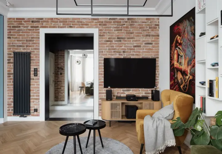 Nowoczesny salon z ceglaną ścianą, na której wisi telewizor. Oświetlenie podkreśla fakturę cegły, tworząc przytulną atmosferę.