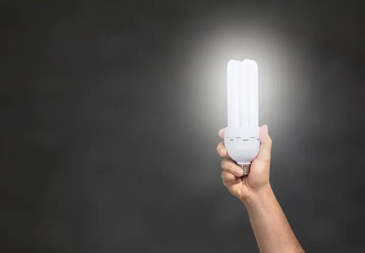 Dłoń trzymająca energooszczędną żarówkę, która świeci jasno. Zastanawiasz się, ile lumenów na m2 zapewni?