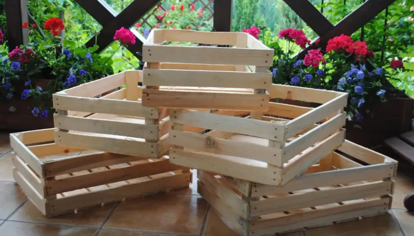 Drewniane dekoracje ze skrzynek po owocach tworzą uroczy zakątek na tarasie, otoczony kwitnącymi kwiatami.
