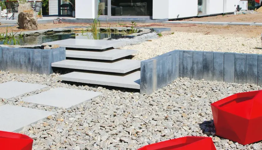 Nowe schody do ogrodu zrób sam, z kamienia i betonu, prowadzą do oczka wodnego.