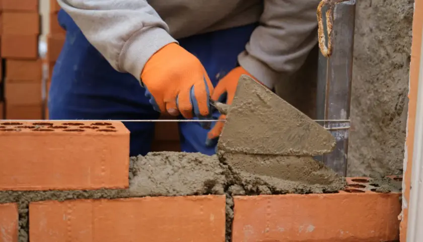 Murarz w pomarańczowych rękawicach układa cegły, tworząc solidny grill z cegły.