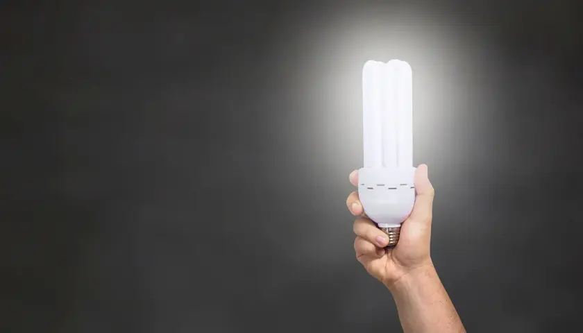 Dłoń trzymająca energooszczędną żarówkę, która świeci jasno. Zastanawiasz się, ile lumenów na m2 zapewni?