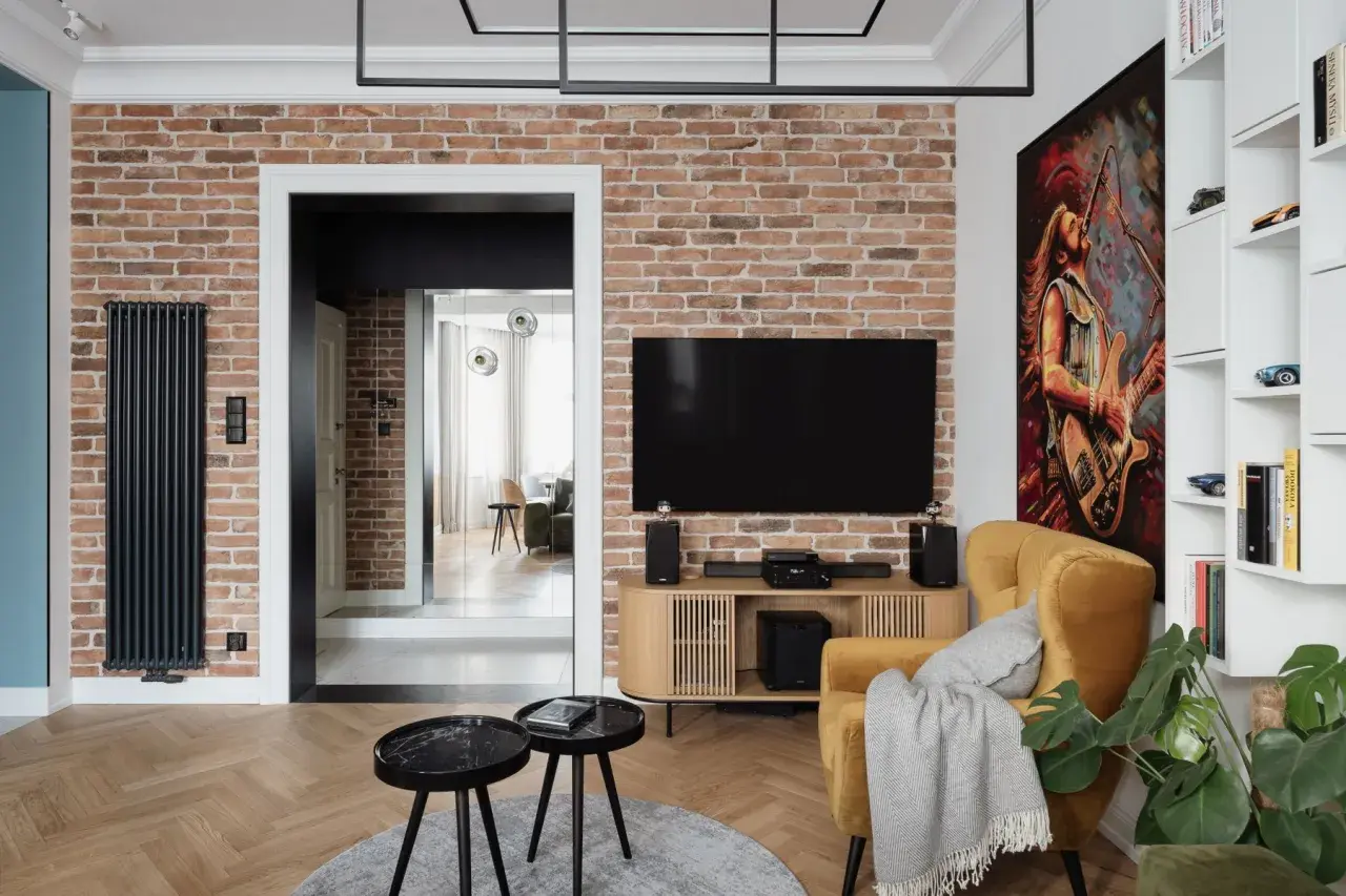 Nowoczesny salon z ceglaną ścianą, na której wisi telewizor. Oświetlenie podkreśla fakturę cegły, tworząc przytulną atmosferę.