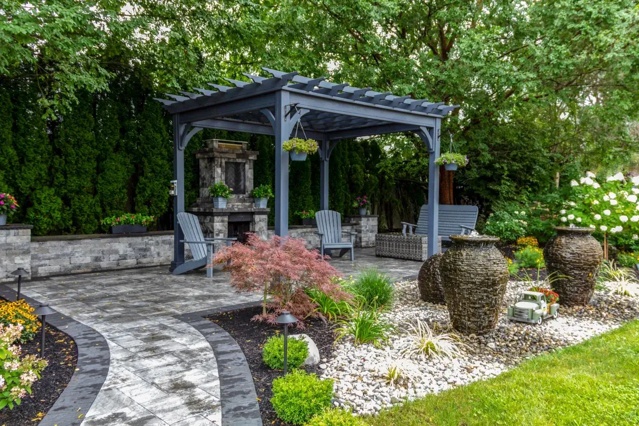 Idealny pomysł na kącik wypoczynkowy w ogrodzie: pergola, kamienny kominek, wygodne fotele i fontanny.