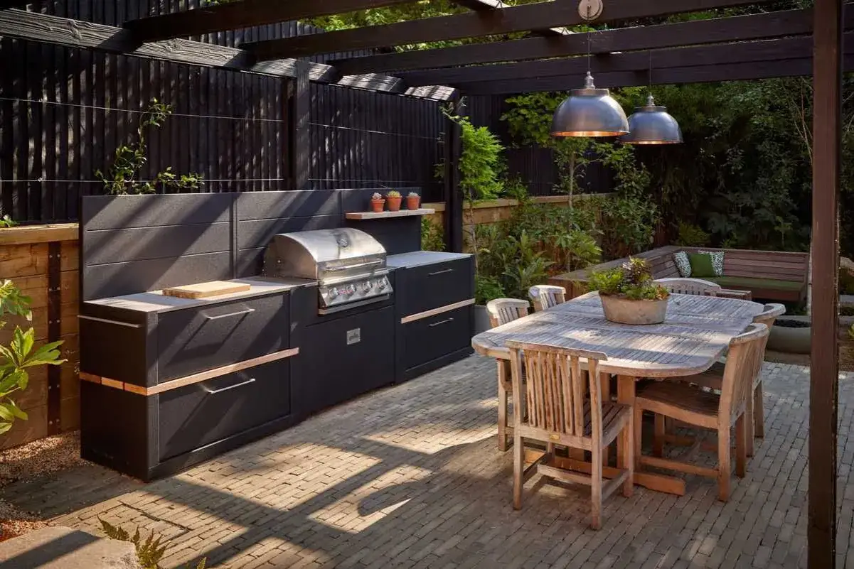 Nowoczesny grill w ogrodzie, gotowy na letnie przyjęcia. Obok stół z krzesłami, idealny do wspólnych posiłków na świeżym powietrzu.